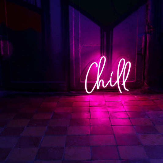 A custom neon light with the text chill on the floor against a wall